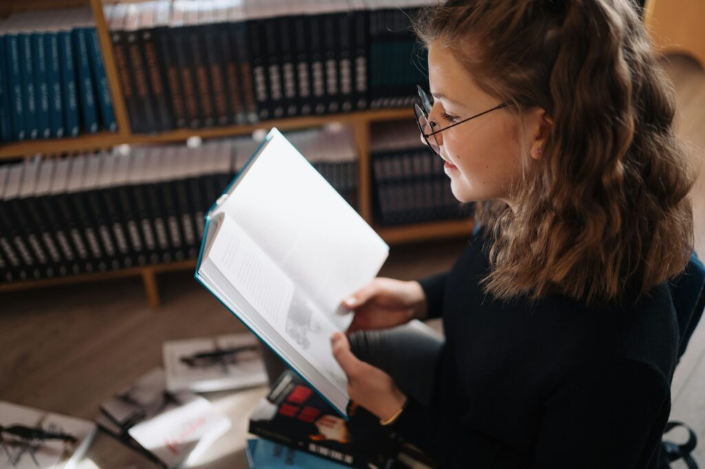 Beautiful girl is studying reading a book while standing on the floor among books in the bookshop